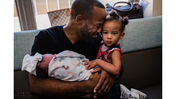 papa étreignant un nouveau-né tout en pleurant et en étreignant sa fille aînée; fille aînée, regardant la caméra