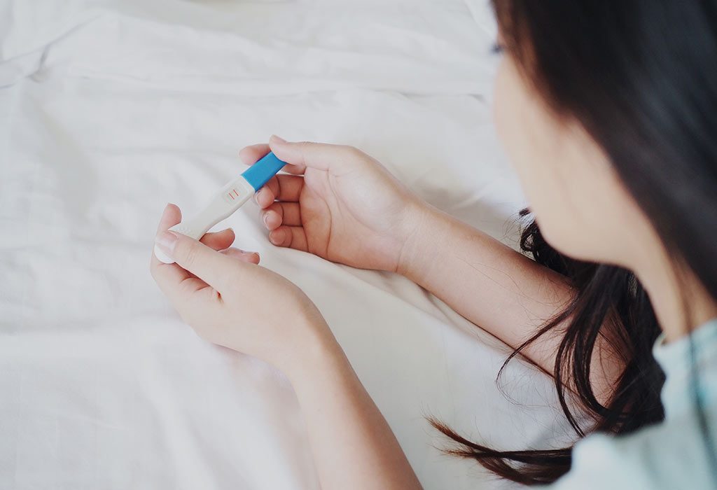 Une jeune femme regarde un bâton de grossesse "width =" 1024 "height =" 700 "srcset =" https://cdn.cdnparenting.com/articles/2018/07/1104137129-H.jpg 1024w, https: // cdn .cdnparenting.com / articles / 2018/07/1104137129-H-768x525.jpg 768w, https://cdn.cdnparenting.com/articles/2018/07/110101313129-H-218x150.jpg 218w, https: // cdn .cdnparenting.com / articles / 2018/07/1104137129-H-696x476.jpg 696w, https://cdn.cdnparenting.com/articles/2018/07/1104137129-H-614x420.jpg 614w "tailles =" (max . -largeur: 1024px) 100vw, 1024px