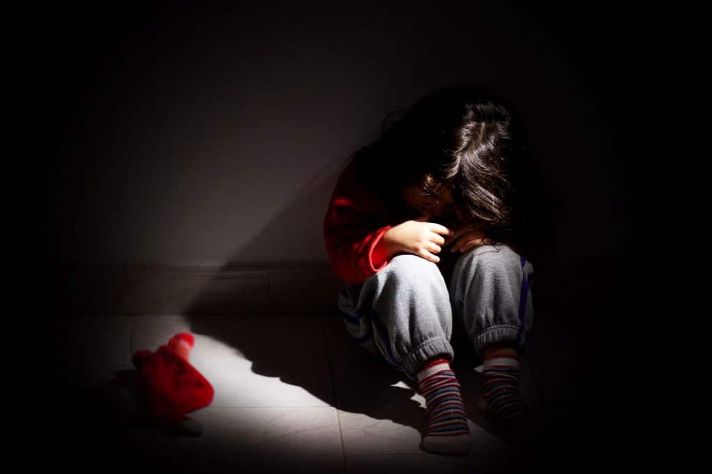 un jeune enfant se blottit dans les ombres sombres d'une pièce vide