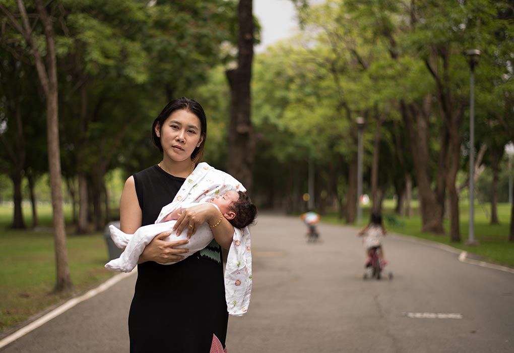Eine Mutter, die ihr 1 Monat altes Baby in einem Park trägt 